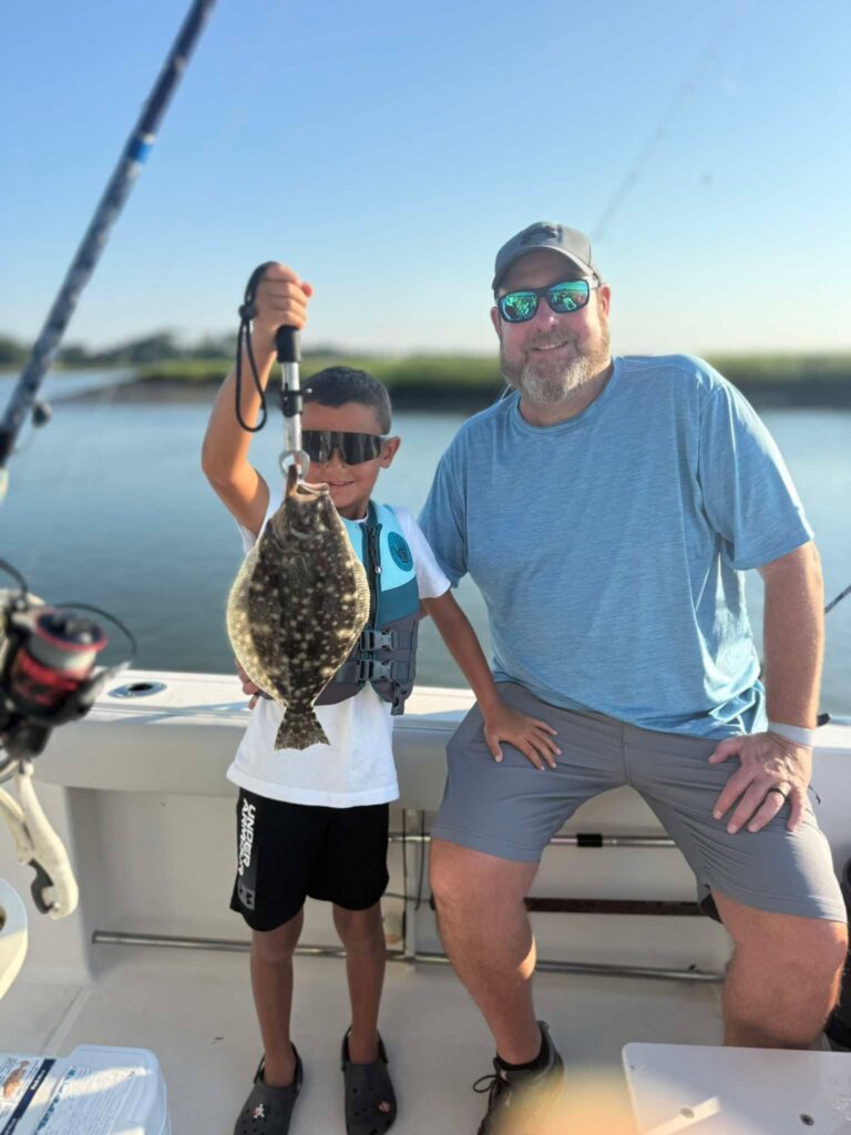 Smiling child holding a flounder beside an adult on a Murrells Inlet fishing boat