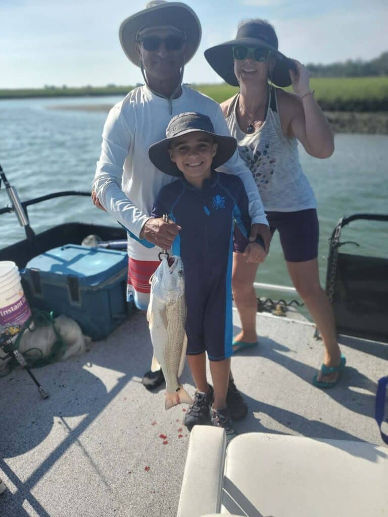 Child holding a redfish with two family members on a Murrells Inlet fishing charter