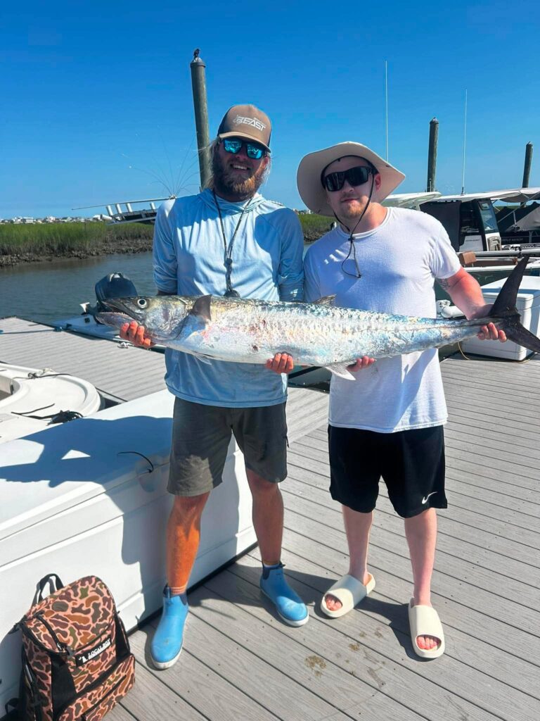 Two anglers holding a large king mackerel on a dock in Murrells Inlet
