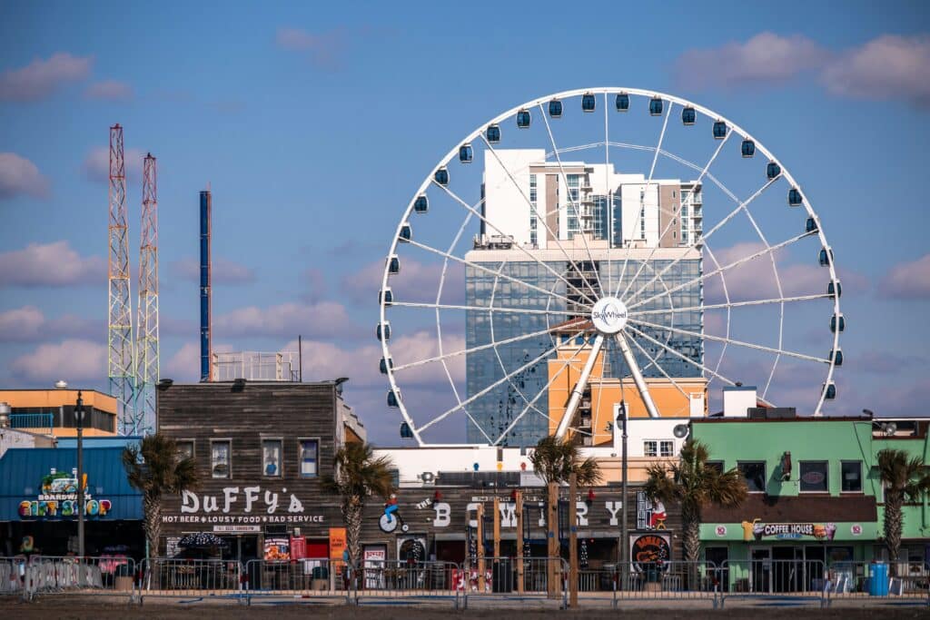 Myrtle Beach SkyWheel above boardwalk businesses under a blue sky