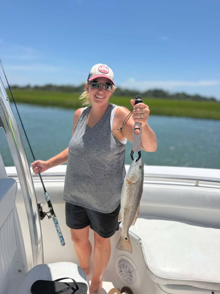 Smiling woman holding a redfish on a boat in the Murrells Inlet marsh