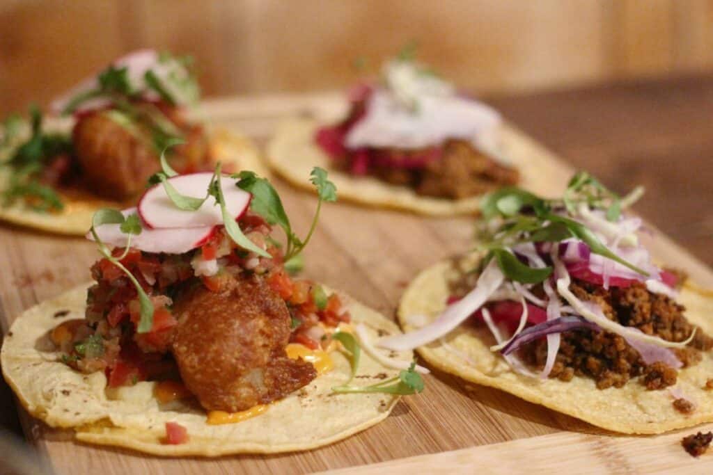 Fried fish tacos topped with salsa, sliced radish, slaw, and fresh greens