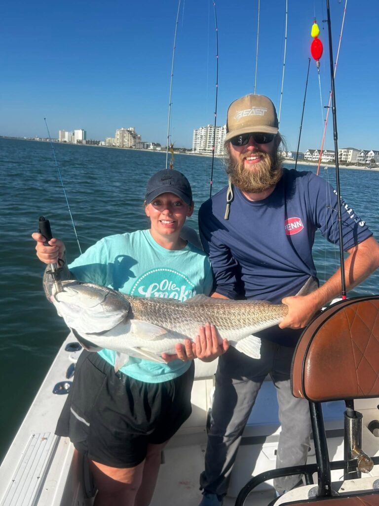 Angler and fishing guide holding a large bull redfish aboard a charter boat near Murrells Inlet