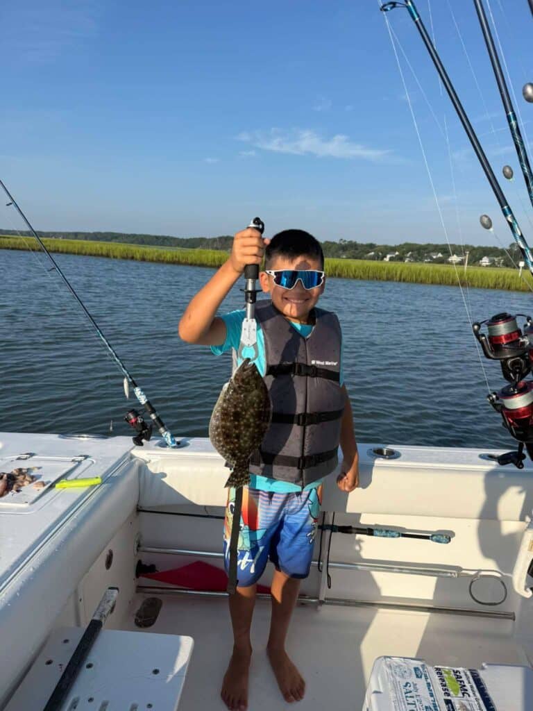 Young angler wearing a life jacket and holding a flounder during a fishing trip in Murrells Inlet